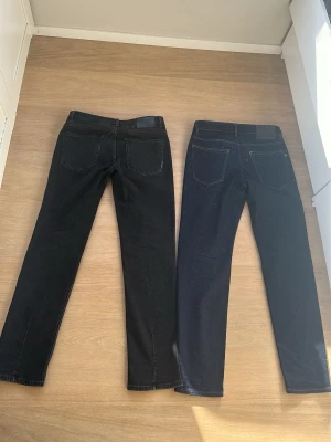 Två par raka jeans i svart och mörkblå - Säljer två par raka jeans, ett par i svart och ett par i mörkblå denim. Klassisk femficksmodell med normal midja och raka ben. Perfekta basjeans för dig som gillar enkel och tidlös stil. Materialet är kraftig bomullsdenim. Ni får båda för 600kr, dem är jättefina och inga slitage eller något. De är väldigt väl skötta. Storlek 30:32 i båda 2