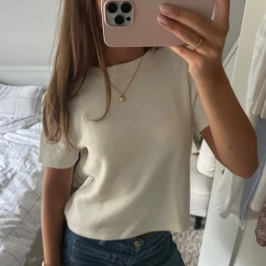 Vit stickad kortärmad topp - Enkel och stilren vit stickad topp med korta ärmar och ribbad rund halsringning. Modellen är rak och något croppad, perfekt till jeans eller kjol. Mjuk och skön känsla i materialet, passar till många olika looks. 