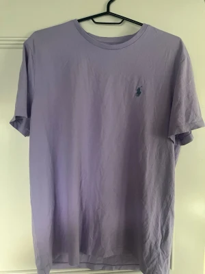 Ljuslila t-shirt från Polo Ralph Lauren - Säljer en ljuslila t-shirt från Polo Ralph Lauren med klassisk passform och korta ärmar. T-shirten har den ikoniska broderade loggan på bröstet och är tillverkad i mjuk bomull. Perfekt till jeans eller shorts för en clean look.