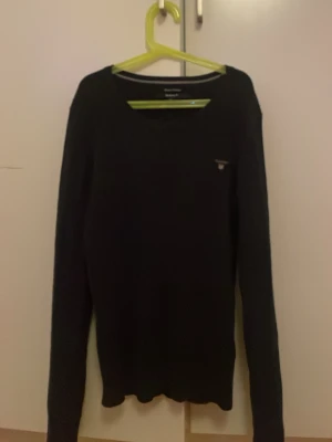 Svart långärmad tröja från GANT - Klassisk svart långärmad tröja från GANT i stretchig bomull. Tröjan har rund halsringning och en liten GANT-logga broderad på bröstet. Enkel och stilren design som passar till det mesta.