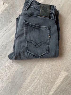 Replay anbass - Säljer ett par gråa slim fit jeans från Replay med snygga detaljer på bakfickan och klassisk femficksdesign. Jeansen har en modern passform som sitter tight längs benen och är tillverkade i mjukt denimtyg för skön känsla. Storlek 29/32