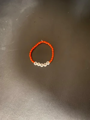 Rött pärlarmband med STARK-bokstäver - Snyggt armband med röda små pärlor och vita bokstavspärlor som stavar STARK. Perfekt accessoar för dig som vill ha något personligt och färgglatt på handleden. Elastiskt band som gör det enkelt att ta på och av.