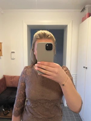 Brun spetsblus med trekvartsärm - Säljer en snygg brun spetsblus med trekvartsärm och rund halsringning. Blusen har ett elegant spetsmönster och är lätt transparent på ärmarna. Perfekt för dig som gillar en feminin och trendig stil.