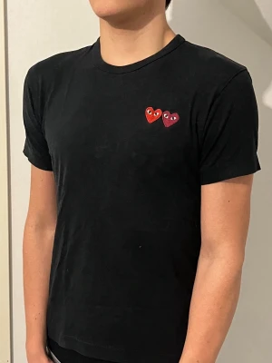 Svart t-shirt från Comme des Garçons - Svart t-shirt från Comme des Garçons. Klassisk rund halsringning och korta ärmar. Det är storlek S på denna t-shirten. Modellen i bilden är 188cm lång och väger 74kg