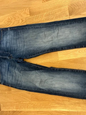 Blå slim fit jeans från Jack & Jones - Mörkblå slim fit jeans från Jack & Jones, modell Slim Glenn. Jeansen har klassisk femficksdesign, snygga slitningar och kontrastsömmar. Tillverkade i stretchigt denimtyg för extra komfort och passform. Perfekta för en avslappnad och trendig stil.