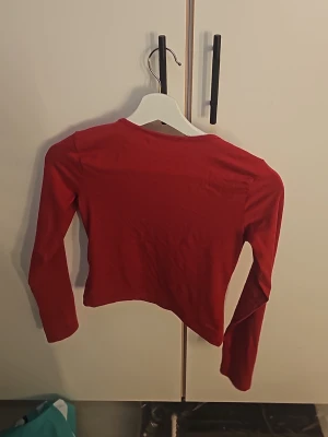 Röd långärmad topp Gina Tricot - Säljer en enkel och snygg röd långärmad topp från Gina Tricot. Modellen är croppad och har en klassisk rund halsringning. Perfekt att matcha med höga jeans eller kjol för en trendig look.