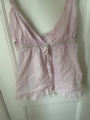 Ljusrosa odd molly topp - Söt ljusrosa linnetopp med volangkant och knytning framtill. Toppen har smala axelband och ett broderat motiv av en fågel på ryggen. Perfekt för varma dagar och ger en romantisk vibe. Har ej koll på vad de kan va för storlek men finns bild på lappen, och skulle säga att den passar en s,🩷