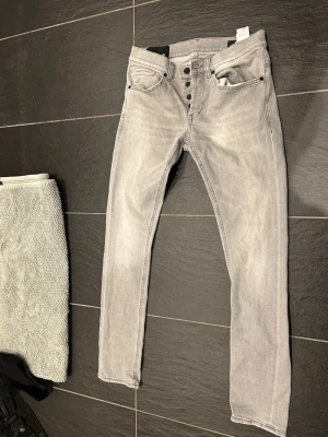 Ljusgrå jeans från dondup  - Säljer ett par ljusgrå slim fit jeans med knappgylf och fem fickor. Jeansen har en snygg tvättad look och raka ben. Materialet är mjukt och stretchigt för extra komfort. Perfekta för en avslappnad och trendig stil. Storlek 30 mycket bra skick 