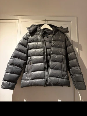 Grå dunjacka från Polo Ralph Lauren - Snygg grå dunjacka från Polo Ralph Lauren. Jackan är i bra skick och det ursprungliga priset var 2500. Skriv vid frågor och funderingar