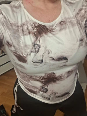 Vit långärmad topp med knyt - Säljer en vit långärmad topp med abstrakt brunt mönster och knyt i sidorna. Toppen har rund halsringning och är croppad i modellen. Perfekt för dig som gillar unika detaljer och en modern look.