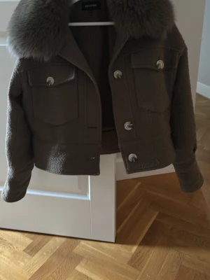 Grön meotine jacka  - Säljer en grön meotine jacka med stor fluffig krager. Jackan har två bröstfickor med lock och är kort i modellen. Perfekt för dig som vill ha en trendig och mysig look. I storlek xs/s. Finns inte att köpa längre!!
