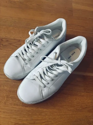 Vita sneakers från Pier One - Klassiska vita sneakers från Pier One med lågt skaft och stilren design. Skorna har vita snören, diskreta sömmar och ovandel i syntetmaterial. Perfekta för dig som gillar en clean och enkel look till vardagsoutfiten.