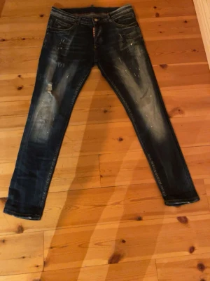 Mörkblå jeans med slitningar - Säljer ett par mörkblå jeans med coola slitningar och blekta detaljer på framsidan. Jeansen har klassisk femficksdesign och raka ben. Perfekt för dig som gillar en avslappnad och trendig look.