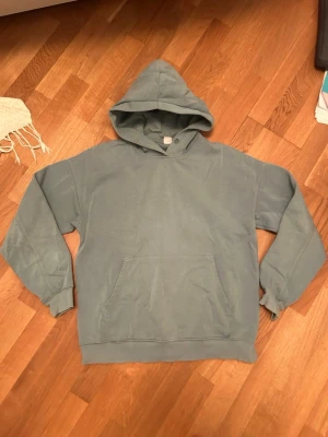 Blå hoodie med huva - En stilren blå hoodie med huva och magficka. Perfekt för en avslappnad look och enkel att matcha med andra plagg. Mjuk bomullskänsla och ribbade muddar vid ärmslut och nederkant.