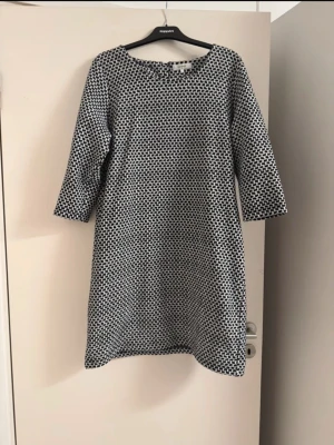 Svartvit mönstrad klänning - En svartvit klänning med grafiskt mönster och trekvartsärm. Klänningen har en rak passform och rund halsringning. Perfekt för dig som gillar enkel men snygg stil.