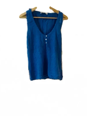 Blå stickad topp med knappar - Snygg blå stickad topp med v-ringning och tre små knappar framtill. Tillverkad i ett lätt, strukturerat tyg som ger en avslappnad känsla. Perfekt att matcha med jeans eller kjol för en trendig look.