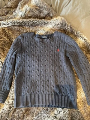 Blå  kabelstickad tröja från Polo Ralph Lauren - Snygg blå  kabelstickad tröja från Polo Raphl Lauren. Tröjan passar 10-12y men skulle säga mellan 150-157cm 