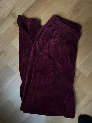 Vinröda mjukisbyxor i velour - Säljer ett par vinröda mjukisbyxor i mjuk velour med resår i midjan och sidofickor. Har även koftan till, så köps i set,  priset nedan är för både kofta samt byxor inte separat 