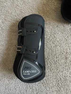 Svarta benskydd Lami-Cell Pro - Säljer två stycket likadana benskydd från Lami-Cell, kolla sista bilden, har även en till annons på dom andra. Dessa har något mer slitage än dom andra. De är ett par svarta benskydd från Lami-Cell Pro, perfekta för större häst. Snygg och sportig design med logga på utsidan.