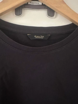 Svart t-shirt från Massimo Dutti - En stilren svart t-shirt från Massimo Dutti med klassisk rund halsringning och korta ärmar. Tillverkad i mjuk bomull som känns skön mot huden. Perfekt basplagg för alla tillfällen och enkel att matcha med olika outfits.