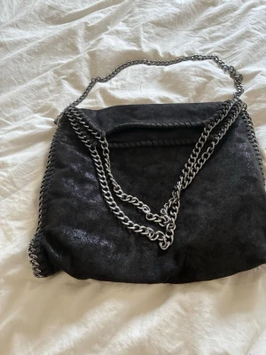 Svart axelväska med kedjedetaljer - Trendig svart väska med kedja💕 en lite större storlek och är perfekt till skolan! Liknar Stella McCartney väskorna, och är knappt använd.