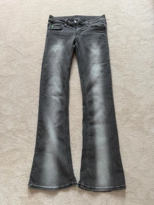 Bootcut jeans från Weekday - Säljer ett par grå bootcut jeans med slitningar och tvättade detaljer. Jeansen har fem fickor och en liten grön detalj på myntfickan. Klassisk knappgylf och raka, utsvängda ben. Perfekta för en avslappnad och trendig look. Strl 29/34 men skulle kunna passa 28 och 27 även. ⭐️