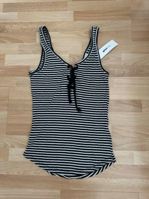 Ny. Randig linnetopp med snörning - Snygg randig linnetopp från Only i svart och vitt med snörning framtill. Toppen är ärmlös och har en v-ringad halsringning. Perfekt för en trendig och avslappnad look.