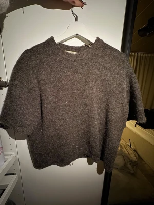 Brun stickad t-shirt från Gina Tricot - Mysig brun stickad t-shirt från Gina Tricot i premiumkvalitet. Tröjan har korta ärmar, rund halsringning och en mjuk, fluffig struktur. Perfekt för lager på lager och en avslappnad look.