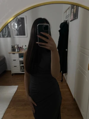 Mörkgrå långklänning med drapering - Säljer en grå lång klänning med draperad detalj på sidan. Klänningen är ärmlös och har en elegant, figurnära passform. Materialet är mjukt och stretchigt, vilket ger en snygg siluett. Perfekt för dig som gillar stilrena och trendiga plagg. Sitter som xs/s använt en gång 