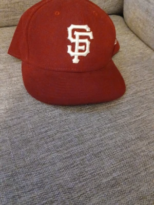 Vinröd keps med vit SF-logga - Snygg vinröd keps med böjd skärm och broderad vit SF-logga framtill. Klassisk basebollmodell som passar perfekt till streetwear. Kepsen har en stilren look och är tillverkad i ett mjukt tygmaterial.