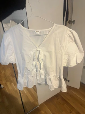Vit blus med puffärm och rosetter - Superfin blus med puffiga ärmar. Storlek 170, skulle säga att det motsvarar ungefär S på den här tröjan. endast använd en gång men säljer för att den är för liten för mig iår. Väldigt fint skick, endast lite skrynklig på bilden❤️