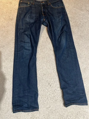 Nudie jeans - Säljer ett par mörkblå jeans från Nudie, modellen är straight alf dry, lappen med storleken har trillat av men jag tror att de är W32 L31, lagning vid skrevet som inte ses alls från utsidan lagat av nudie I deras butik. Tveka inte på att fråga om du har några funderingar🤗