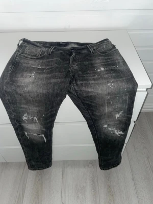 Svarta slitna jeans med tvättade detaljer - Säljer ett par svarta jeans med coola slitningar och tvättade detaljer. Jeansen har fem fickor, normal midja och smal passform. Perfekta för dig som gillar en avslappnad och trendig stil. Materialet är klassisk denim med stretch.