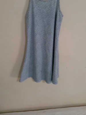 Ljusblå ärmlös klänning med mönster - Söt ljusblå klänning med ärmlös design och små vita och svarta blommönster över hela tyget. Klänningen har en rak, lätt utställd passform och är tillverkad i ett mjukt, bekvämt material. Perfekt för dig som gillar en enkel men stilren look.