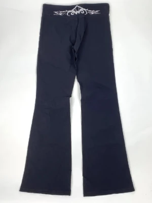 Svarta bootcut leggings - Snygga svarta leggings med bootcut passform. De har ett vitt tribal-inspirerat mönster på linningen och är tillverkade i ett mjukt och stretchigt material som ger en bekväm känsla. 