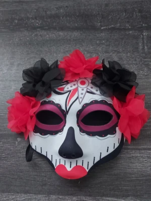 Svart mask med röda och svarta blommor - Maskeradmask i svart plast med elastiskt band och stora dekorativa blommor i rött och svart tyg. Perfekt för cosplay, halloween eller temafest där du vill sticka ut med en dramatisk look.