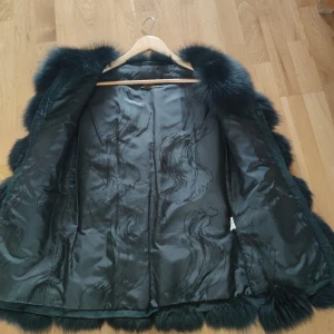 Svart fluffig pälsväst - Säljer en svart pälsväst med riktigt fluffig och voluminös look. Västen har breda, mjuka sektioner av päls och en elegant, mönstrad insida. Perfekt för dig som vill sticka ut med en lyxig och trendig stil. Västen är ärmlös och har en rak passform.