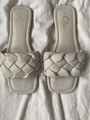 Vita flätade sandaler från Chloé - Säljer ett par trendiga vita sandaler från Chloé med breda, flätade remmar och fyrkantig tå. Tillverkade i mjukt konstläder som ger en clean och modern look. Perfekta för sommarens alla outfits. Passar även mig fortfarande och jag har storlek 37-38 nu.💘