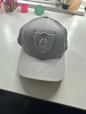 Grå Raiders keps från New Era - Snygg grå keps från New Era med Raiders-logga broderad framtill. Modellen är 9FIFTY med justerbar snapback och böjd skärm. Perfekt för dig som vill ha en stilren och sportig look. Materialet är bomullsmix som känns bekvämt hela dagen.