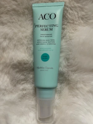 ACO Perfecting Serum ansiktsserum - ACO Perfecting Serum är ett ansiktsserum i en mintgrön plasttub med pump. Innehåller niacinamid och hyaluronsyra som jämnar ut hudtonen, förbättrar hudens struktur och återfuktar på djupet. Tuben har svart text och en rund blå detalj på framsidan.