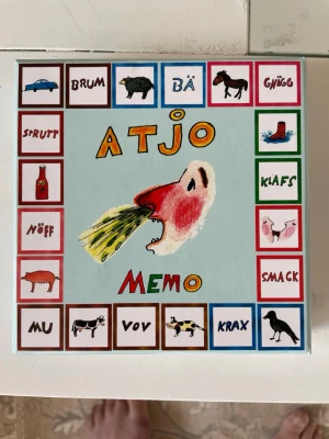 Atjoo Memo spel med ljud och bilder - Säljer ett roligt memo-spel som heter Atjoo, där man parar ihop kort med ljud och bilder. Spelet har färgglada illustrationer av djur, ljud och olika saker. Perfekt för att träna minnet och ha kul tillsammans! Lådan och korten är i papp med lekfull design.barnen lär sig att enkelt att läsa 