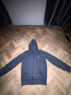 Mörkblå hoodie från Polo Ralph Lauren - Snygg mörkblå hoodie från Polo Ralph Lauren med dragkedja framtill och klassisk huva. Tröjan har två fickor fram och den ikoniska lilla loggan broderad på bröstet. Perfekt för en avslappnad och stilren look. Tillverkad i mjukt bomullsmaterial. Size:XS. Mer tröjor finns in min profil. Köpte den för 2.400kr säljer den billigt