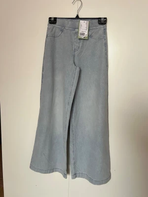 Ljusblå wide leg jeans från H&M - Säljer ett par ljusblå wide leg jeans från H&M med hög midja och raka, vida ben. Jeansen har klassisk femficksdesign och är gjorda i mjukt ,stretchat denimtyg.Resorband i midjan Perfekta för en avslappnad och trendig look.Djur och rökfritt hem 