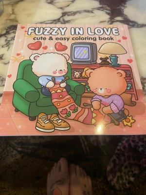 Fuzzy in Love målarbok - En söt och enkel målarbok med titeln 'Fuzzy in Love'. Omslaget har gulliga björnar i pastellfärger och boken innehåller flera illustrationer att färglägga med kärlekstema. Perfekt för dig som gillar kawaii och kreativa aktiviteter.