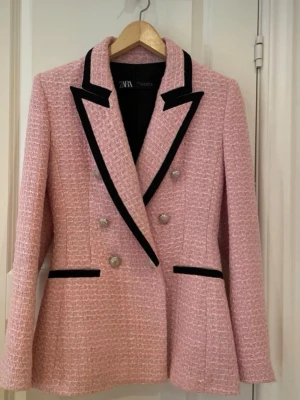 Rosa tweedkavaj/tweedjacka Zara - Stilren rosa kavaj från Zara i tweedliknande material med markerade svarta kanter på slag och fickor. Dubbelknäppt med silvriga knappar och figurnära passform. Perfekt för dig som vill sticka ut med en trendig och elegant look. Obetydligt använd.