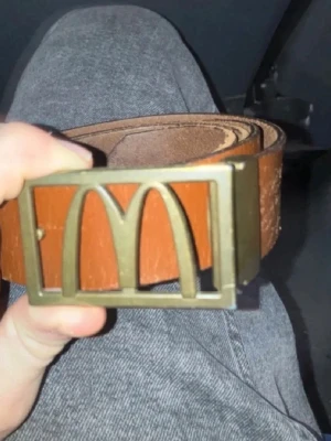 McDonald’s bälte - Snyggt brunt skärp från mcdonalds med ett unikt metallspänne som har en cool design. Skärpet är gjort i skinn och har en klassisk look som passar till jeans eller byxor. Perfekt accessoar för att lyfta din outfit.