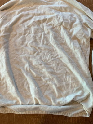 Vit basic långärmad tröja - En enkel vit långärmad tröja i mjukt och tunt material. Tröjan har rund halsringning och ribbade muddar vid ärmslut och nederkant. Perfekt som basplagg till olika outfits.