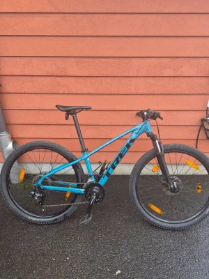 Blå mountainbike från Trek XS - Trek mountainbike för herr med ramstorlek XS och 27,5" hjul. Cykeln har en hård framgaffel med dämpare, raka styren och grovmönstrade däck anpassade för terrängkörning. Färgen är blå med svarta detaljer. Passar för stigcykling, pendling och vardagsbruk på varierande underlag. Den har 7 växlar bak och 3 växlar fram