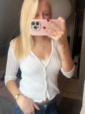 Vit stickad kofta med knappar - Snygg vit stickad kofta med trekvartsärmar och knäppning framtill. Koftan har ett luftigt hålmönster och en kortare passform som passar perfekt till jeans eller kjol. Materialet känns mjukt och lätt. Finns en litet hål (se sista bild) men de är inget som märks av. 