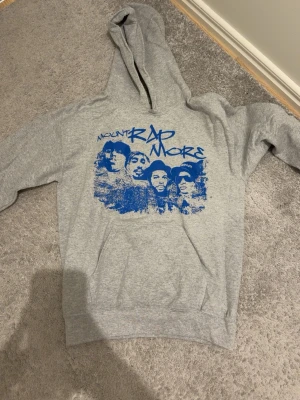 Grå hoodie Mount Rap More tryck - Snygg grå hoodie från Gildan med blått Mount Rap More-tryck på bröstet. Klassisk passform med huva och känguruficka framtill. Tillverkad i mjuk bomullsblandning som är skön att ha på sig. Perfekt för dig som gillar streetwear och unika prints.